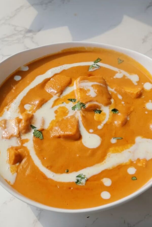 Homemade butter paneer masala in a white bowl with cream and cilantro.