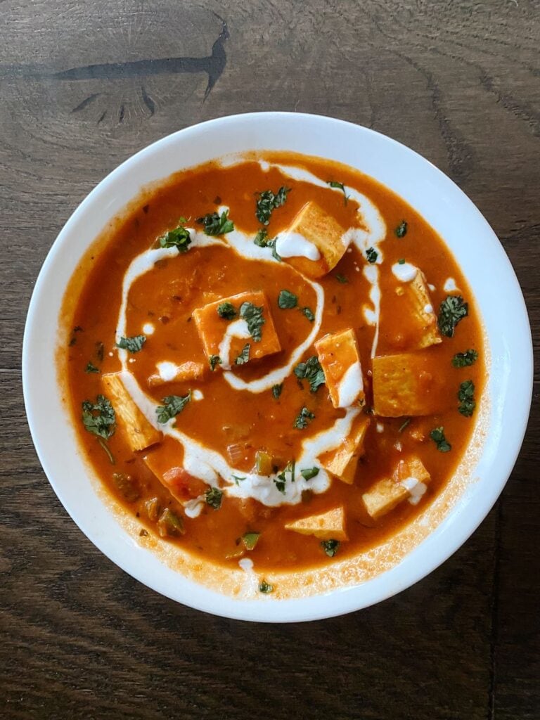 paneer makhani in a bowl on a hardwood floor backdrop