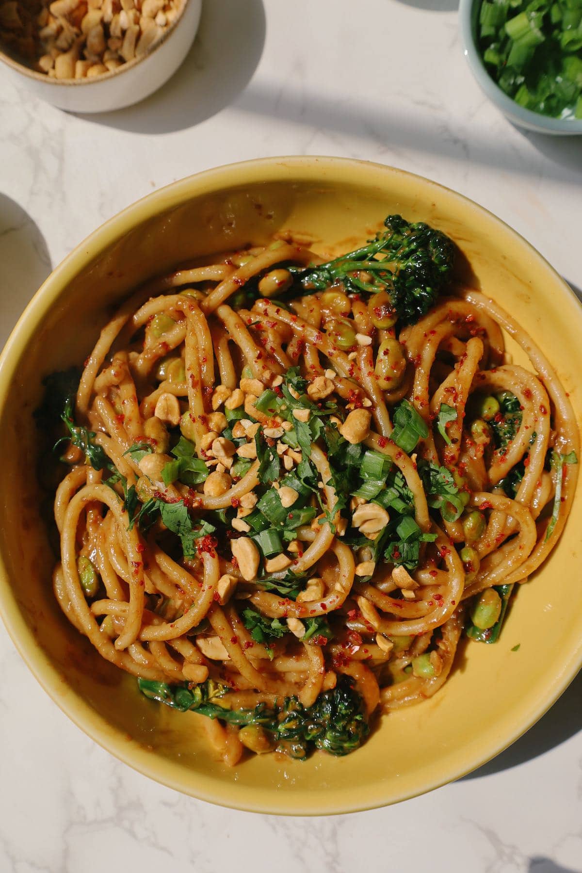 Spicy peanut noodles in a bowl with scallions and cilantro on top.