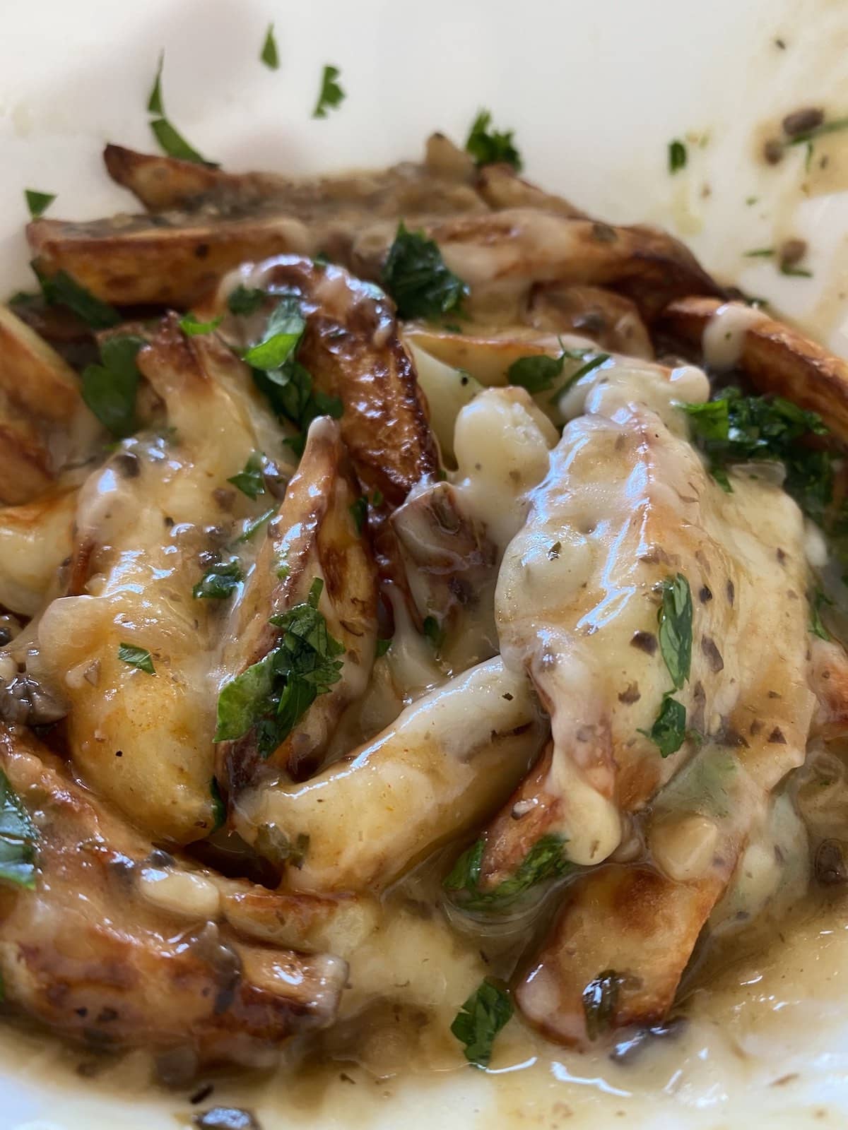 Close-up of golden potato wedges topped with thick creamy mushroom gravy, melted vegan cheese and parsley.