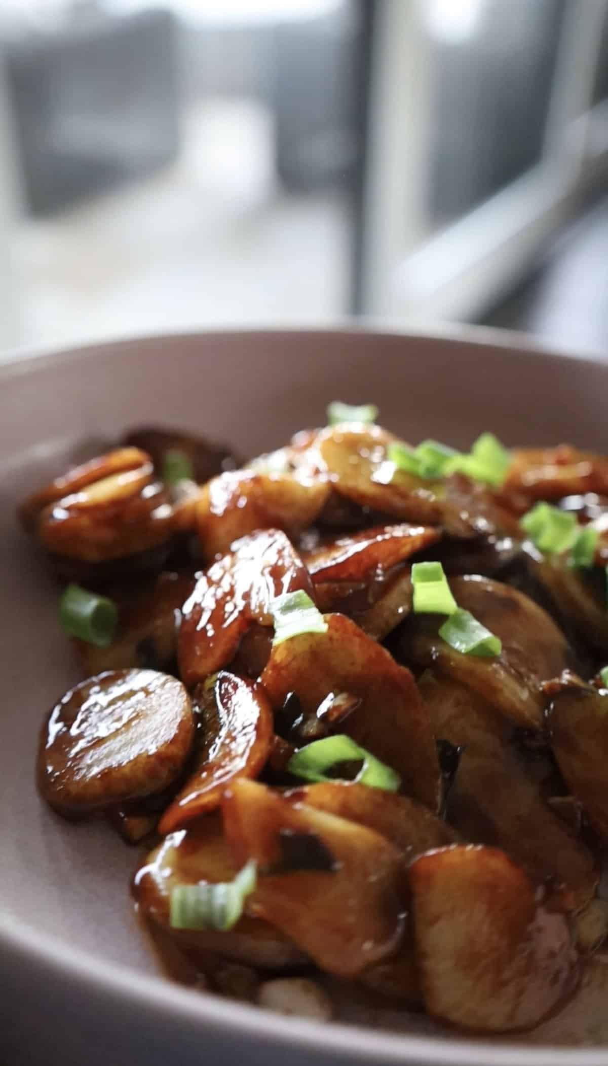 Close-up of stir-fried Shanghai rice cake slices in dark sauce with chopped scallions.