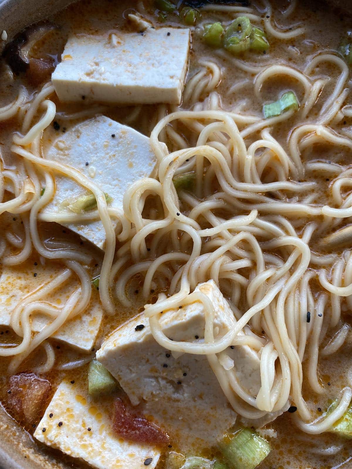Close-up of creamy vegan ramen broth with tofu, scallions, and seaweed.