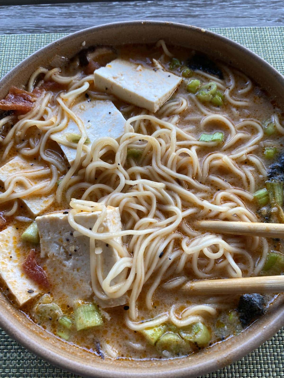 A bowl of vegan ramen with chopped green onions, tofu cubes and sliced peppers in a creamy broth.