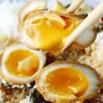 Mayak eggs with a runny yolk over eggs.
