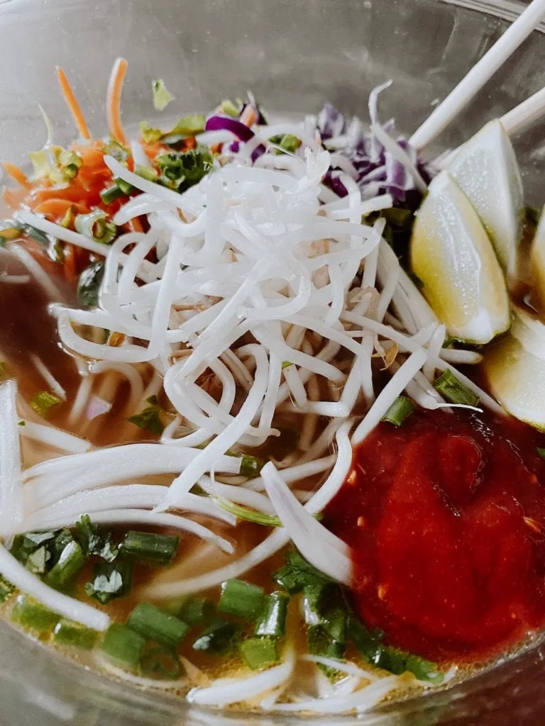 toppings including bean sprouts, limes, and veggies.