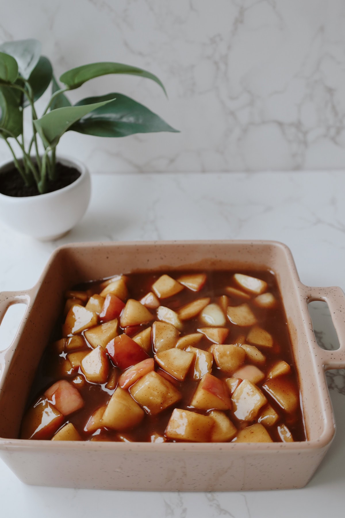 Chopped apples in cinnamon-brown sugar sauce inside a rectangular baking dish before topping.