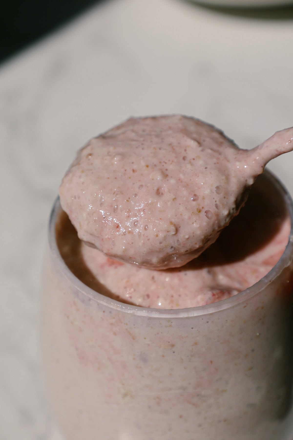 Spoon lifting a thick scoop of pink blended strawberry overnight oats from a glass.