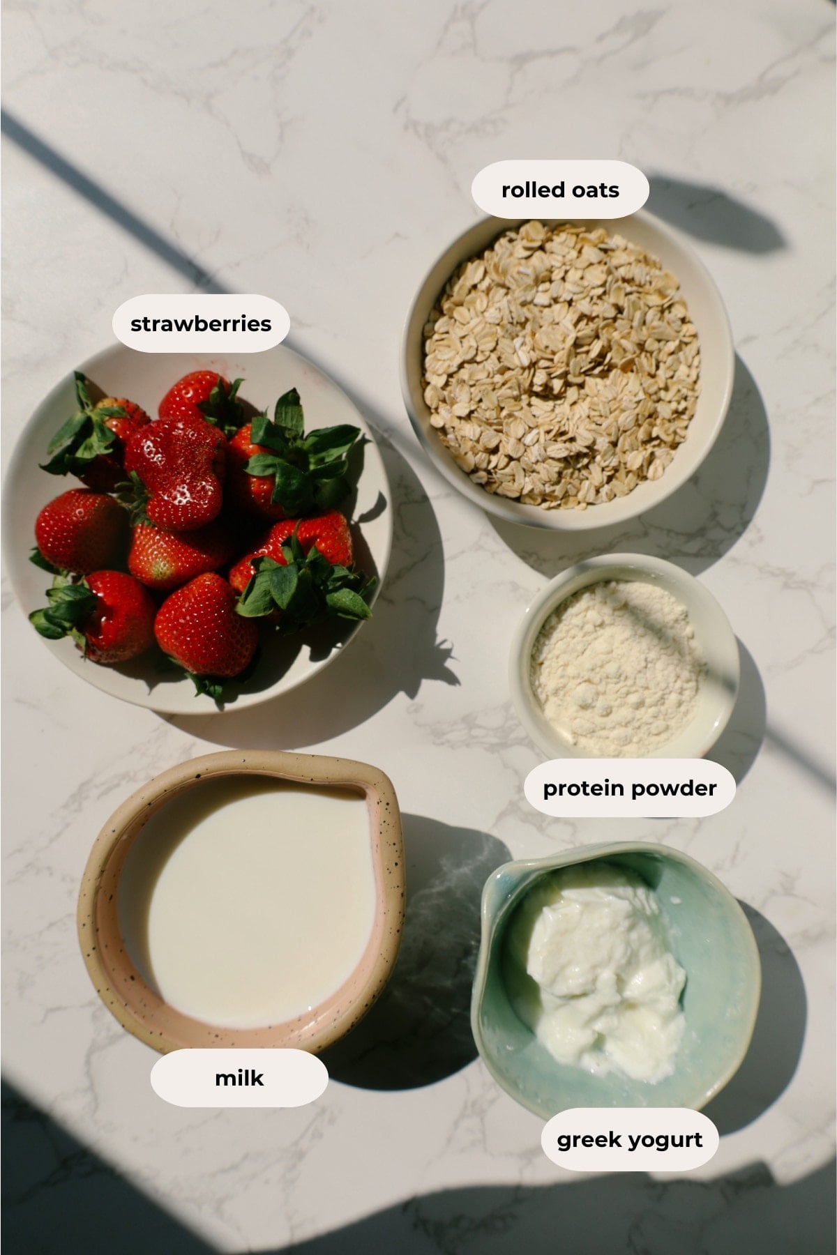 Overhead ingredient layout labeled strawberries, rolled oats, protein powder, milk, and Greek yogurt.