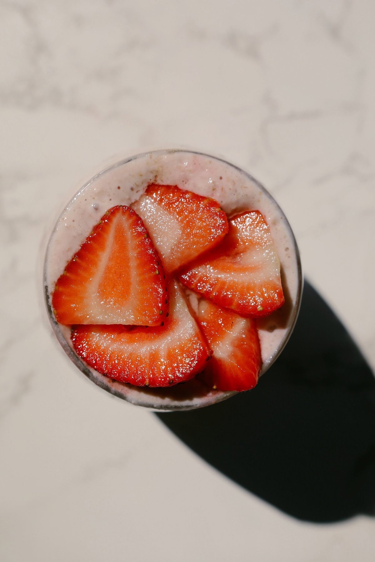 Glass of creamy pink strawberry overnight oats with red strawberry swirls and sliced berries on top.