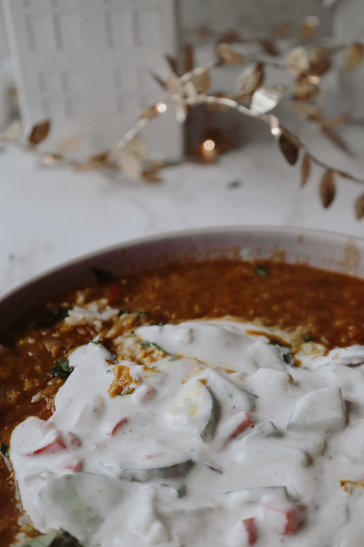 Close-up of white cucumber and tomato yogurt raita spooned over spiced lentils.