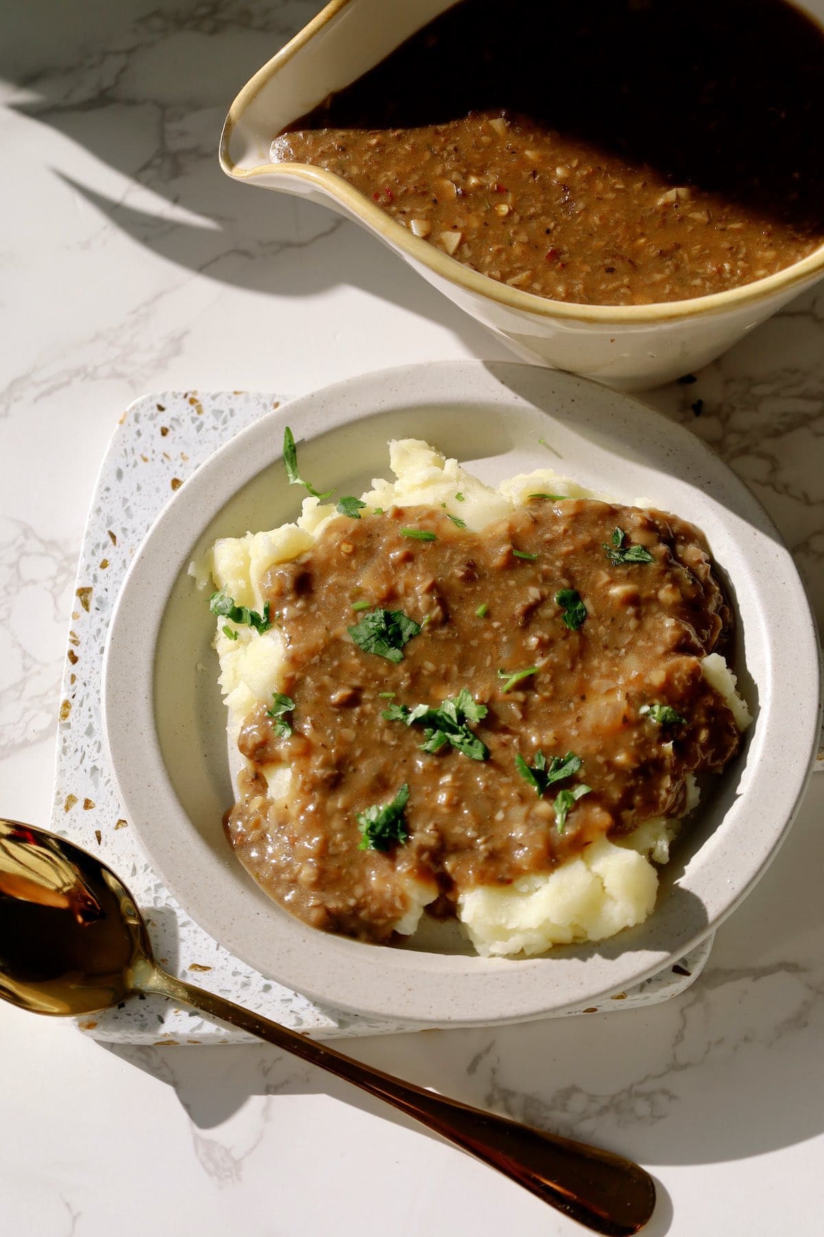 A plate of creamy mashed potatoes topped with lots of mushroom gravy, a mushroom gravy boat on the side.