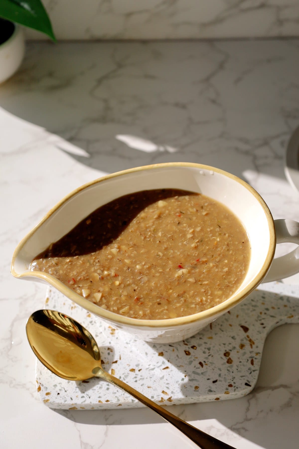 Creamy mushroom gravy in a white gravy boat beside a gold spoon.