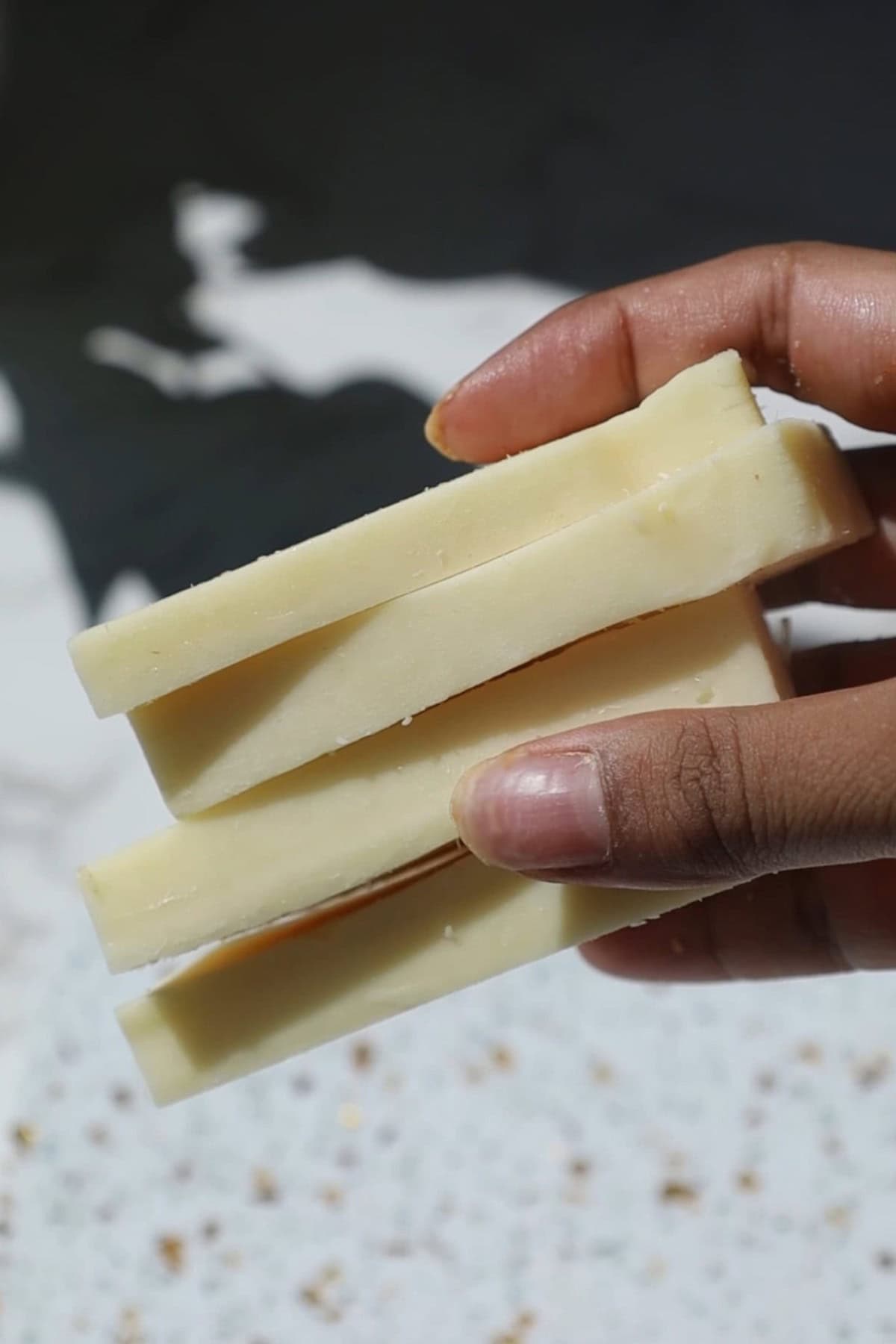 Low moisture mozzarella slices in someone's hand.