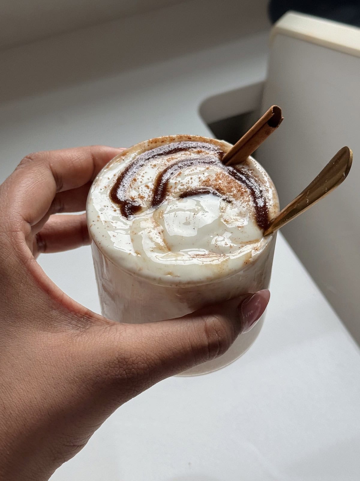A hand holding a cup of cinnamon roll overnight oats.