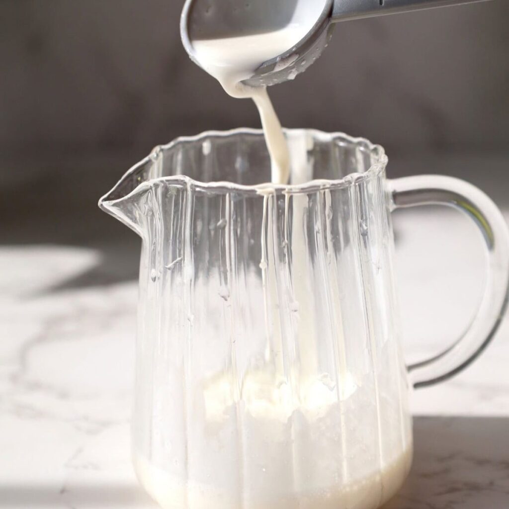 a small clear ribbed jug being filled with milk.