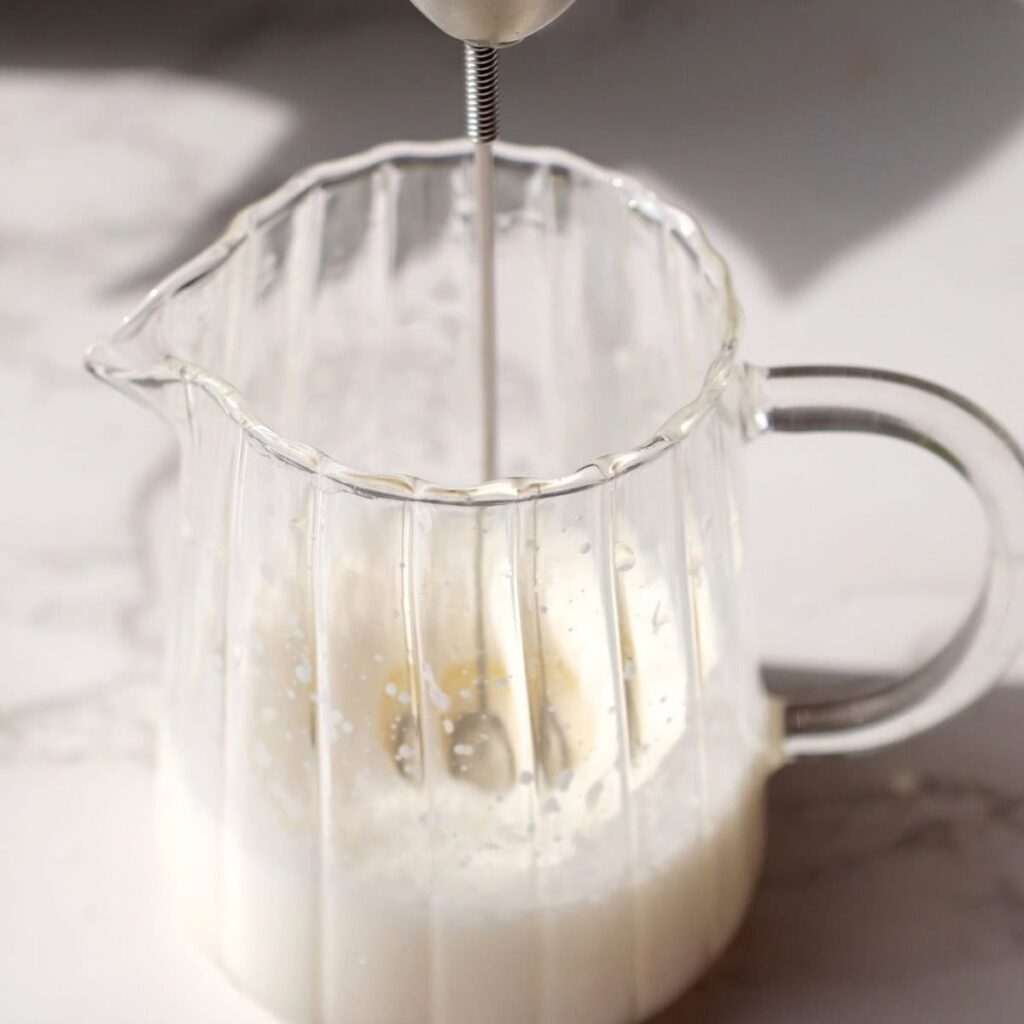 a milk frother in a jug with milk and heavy cream.