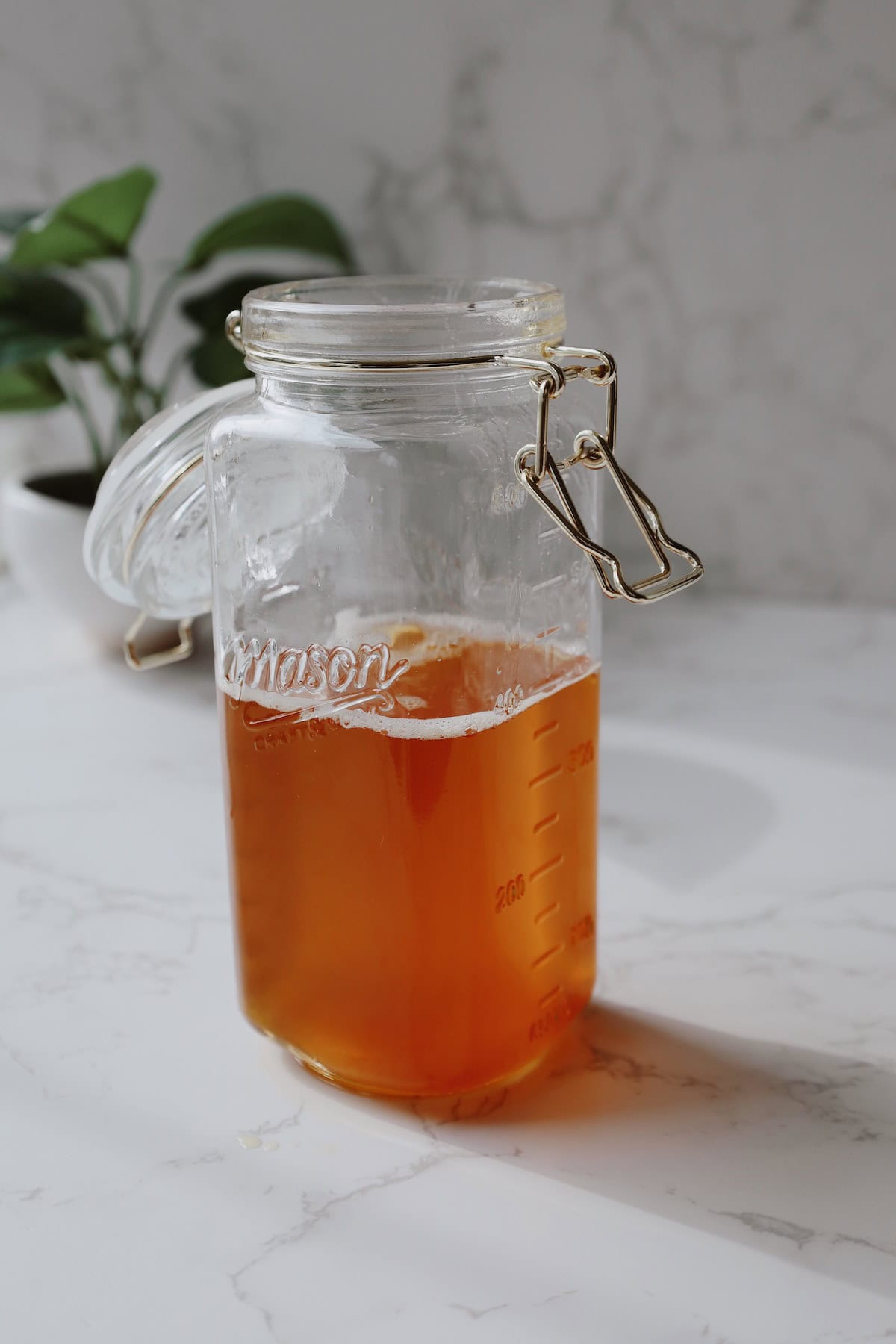 Clear glass clip-top jar partly filled with amber homemade ghee on a marble countertop.