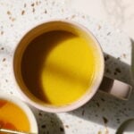 Golden milk in a cup next to a small bowl of honey.