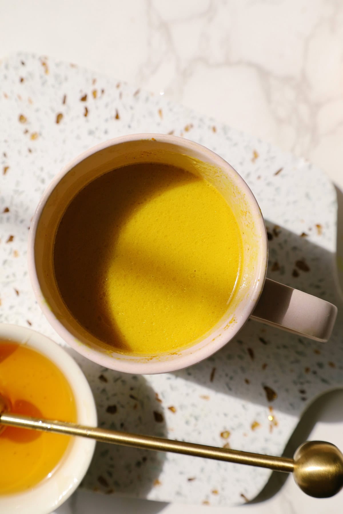 Golden milk in a cup next to a small bowl of honey.