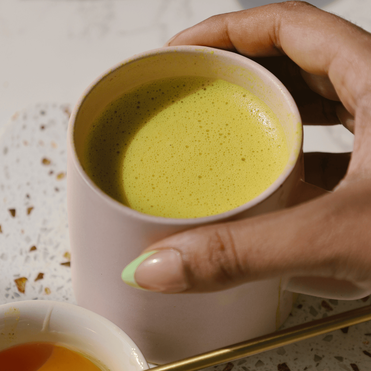 Hand holding a pink cup filled with golden milk.