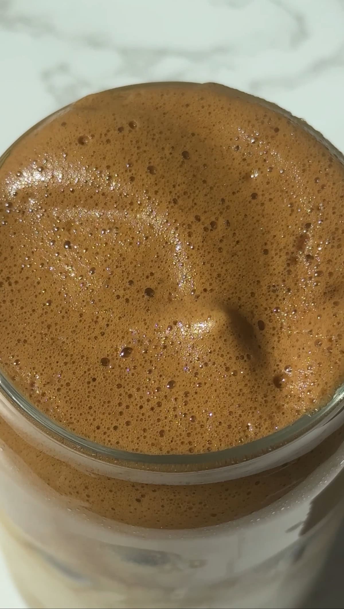 Whipped honey coffee foam at the surface of the glass.