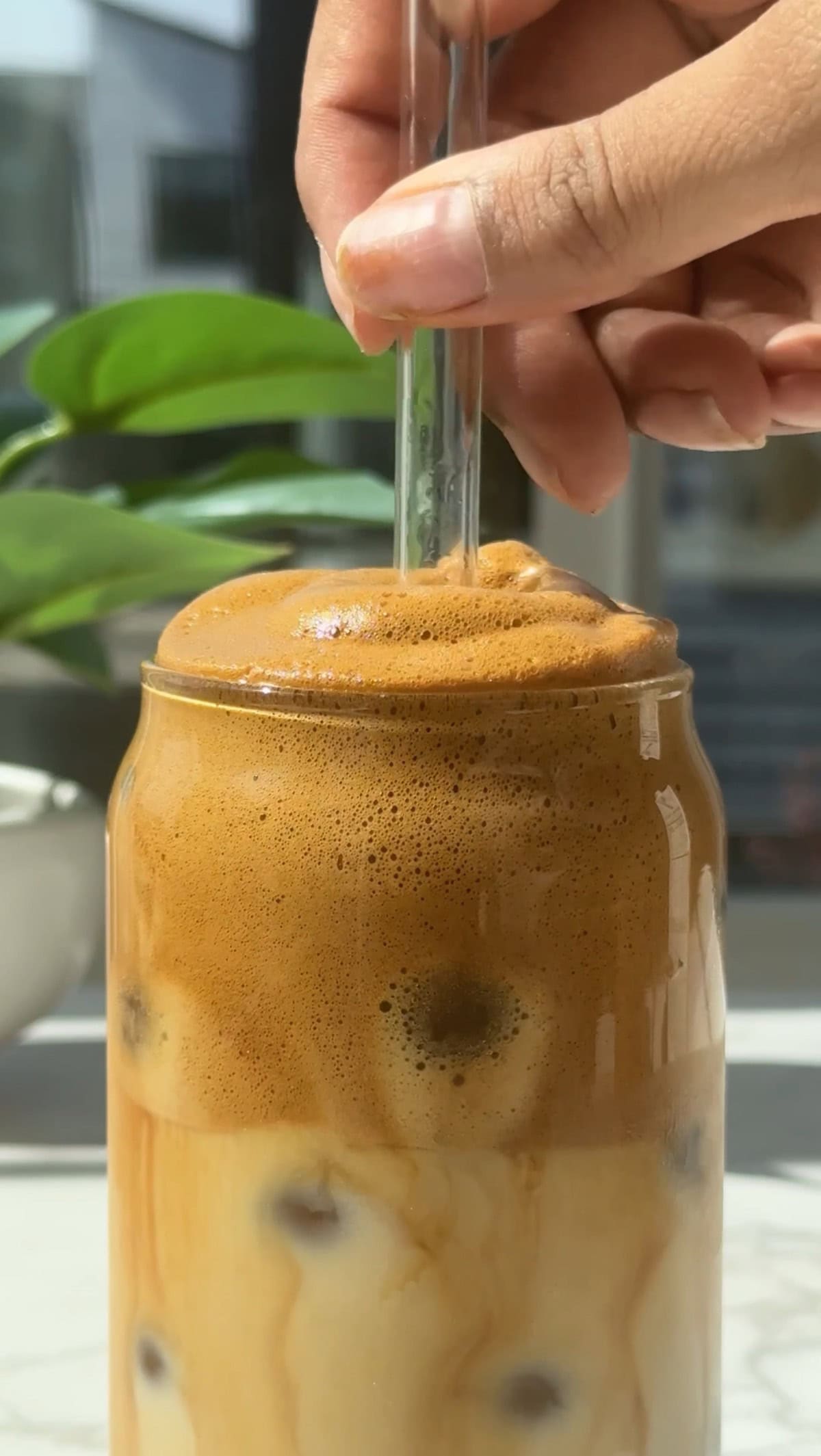 Whipped honey coffee in a glass with a clear straw inside it.