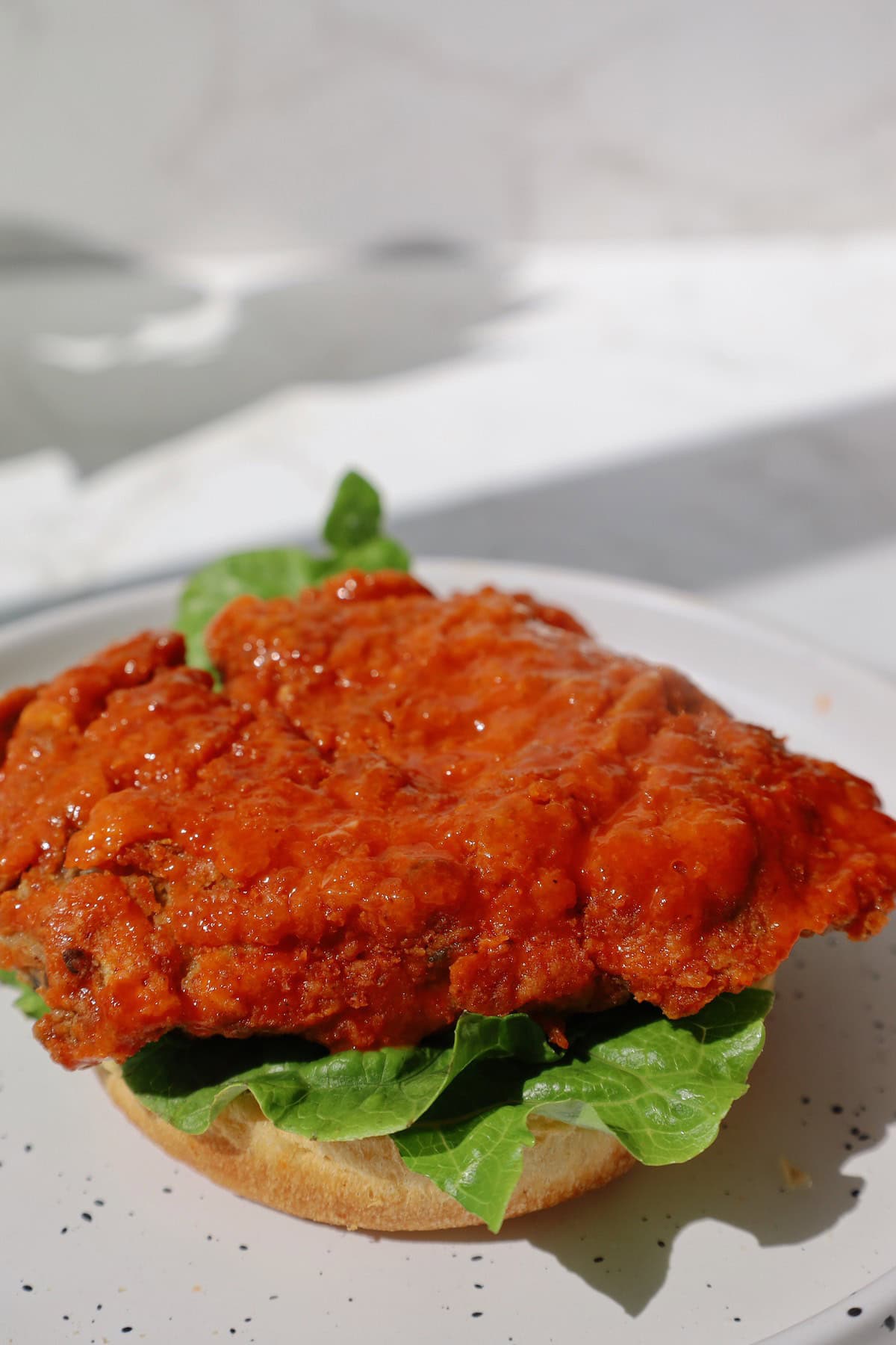 Crispy oyster mushroom patty coated in orange buffalo sauce resting on romaine lettuce and the bottom half of a bun.