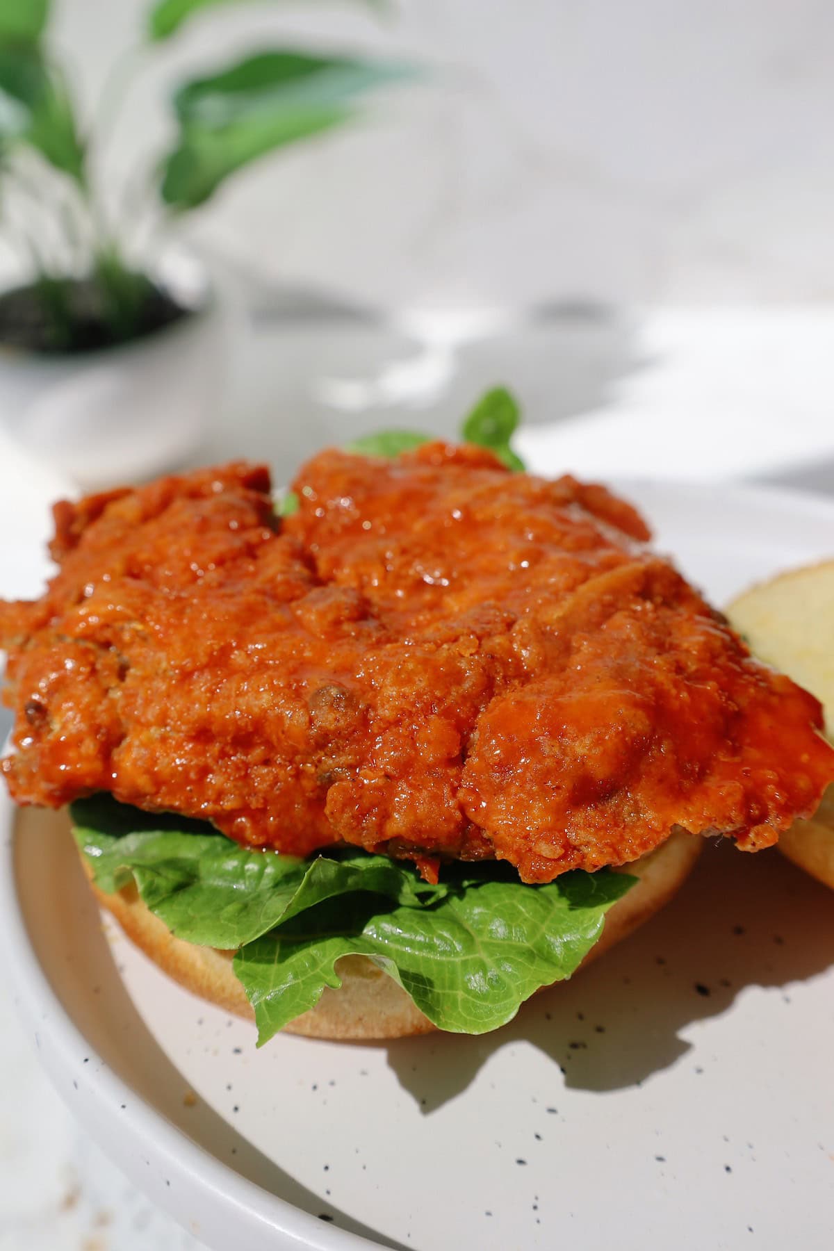 Close-up of a buffalo-coated crispy oyster mushroom burger patty on lettuce and a bottom bun.