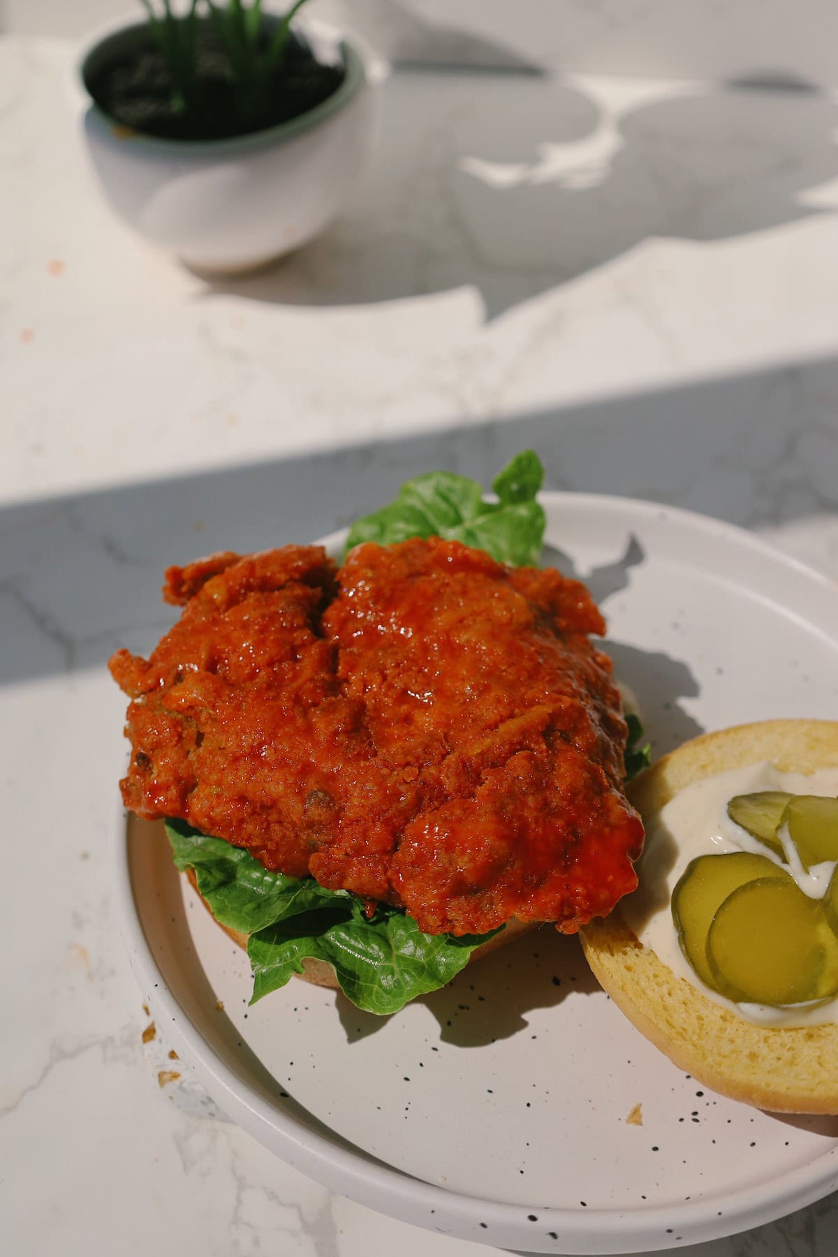 Open buffalo mushroom burger with a glazed crispy patty over lettuce and the top bun spread with ranch and pickles.