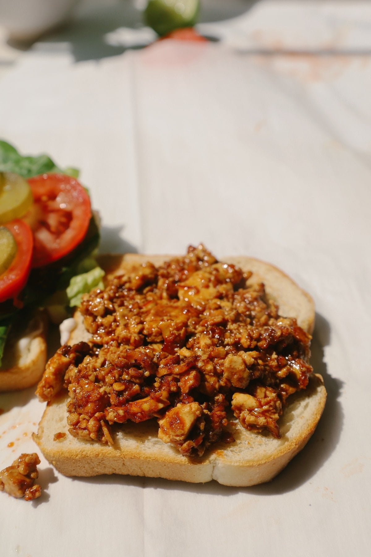 Close-up of spiced, crumbled tofu piled onto a slice of sourdough beside lettuce, tomato and pickles.