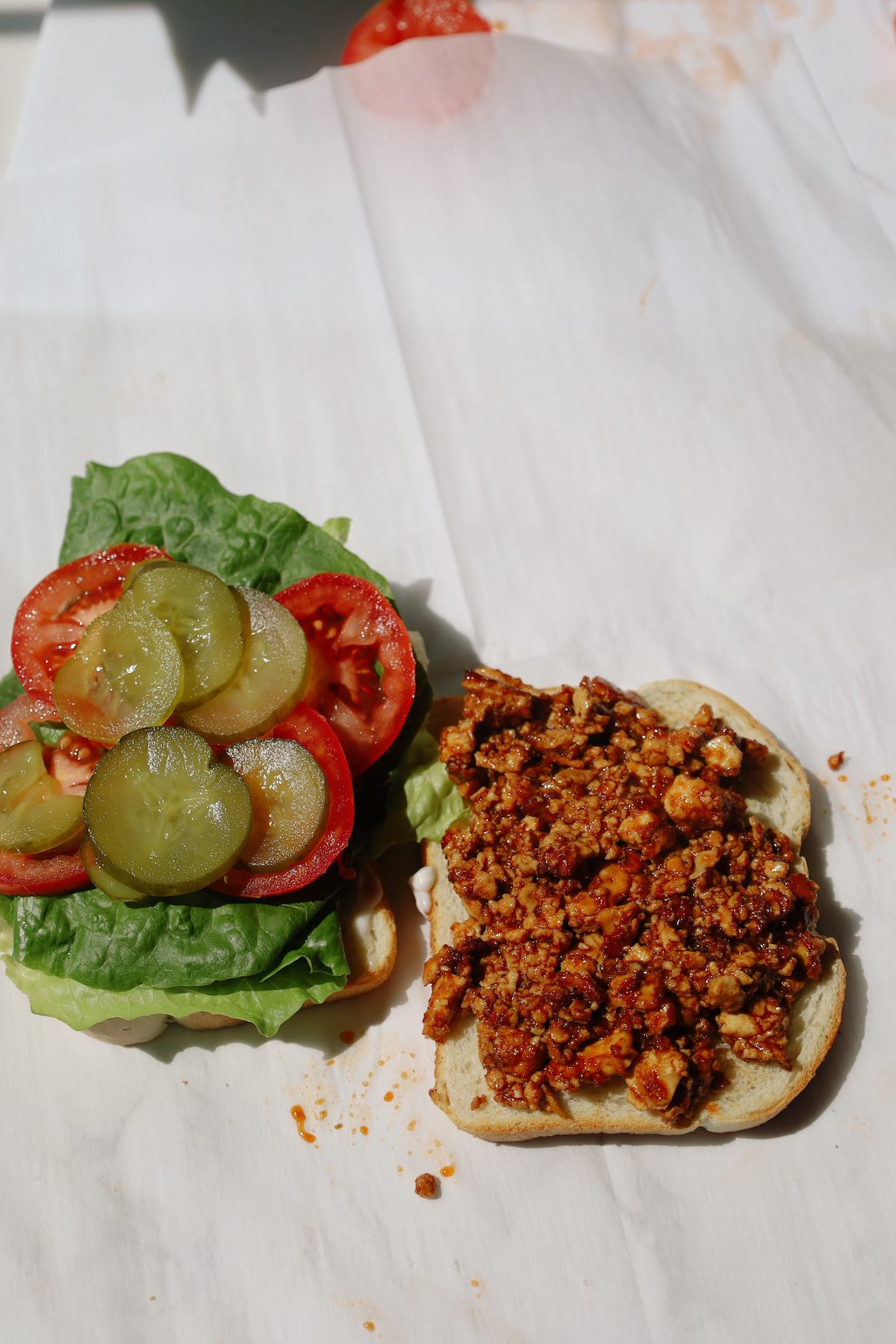 Open-faced tofu sandwich with seasoned crumbled tofu on one slice and lettuce, tomato and pickles on the other.
