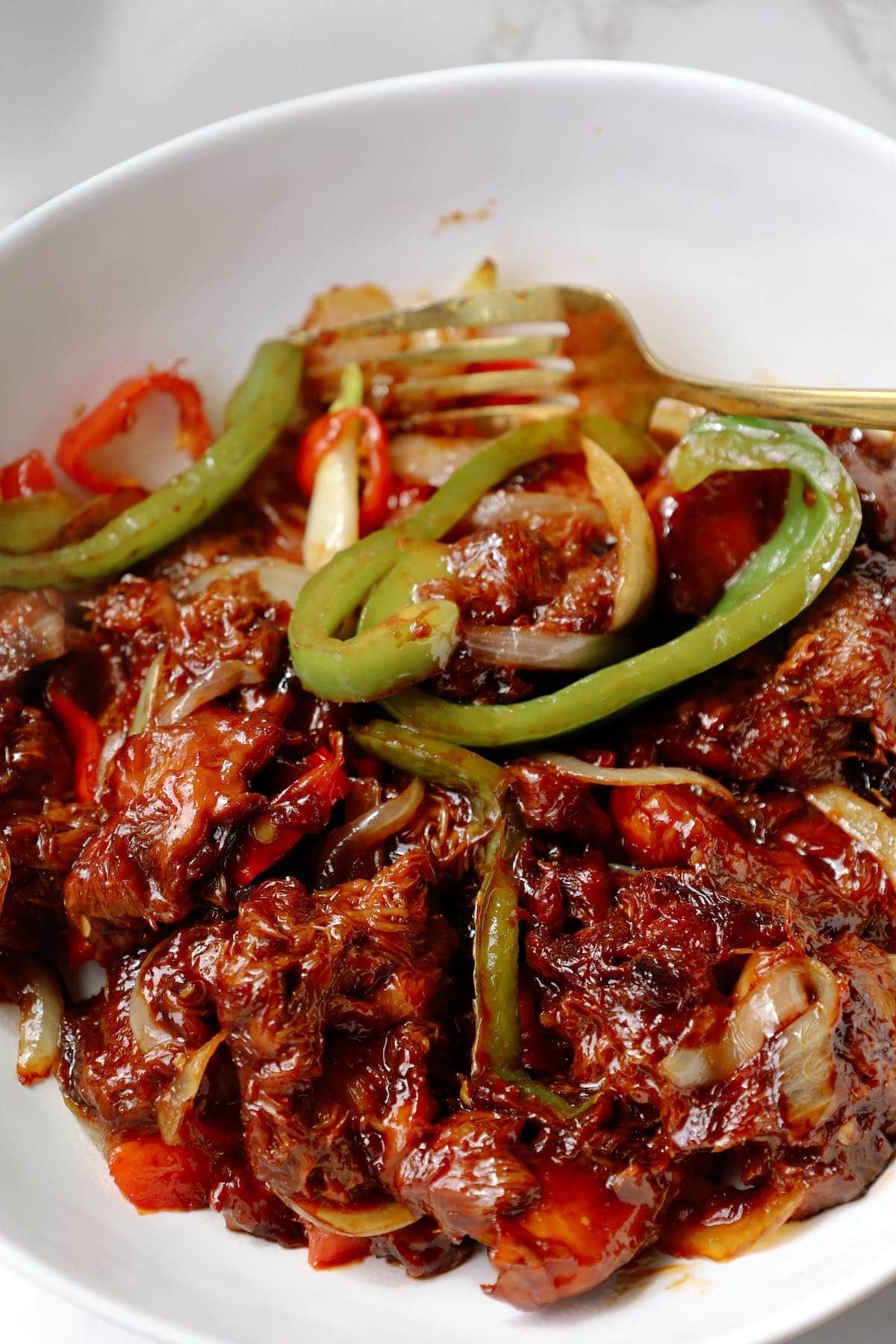Close-up of glossy sweet chilli lion’s mane mushroom pieces with green peppers and onions in a white bowl.