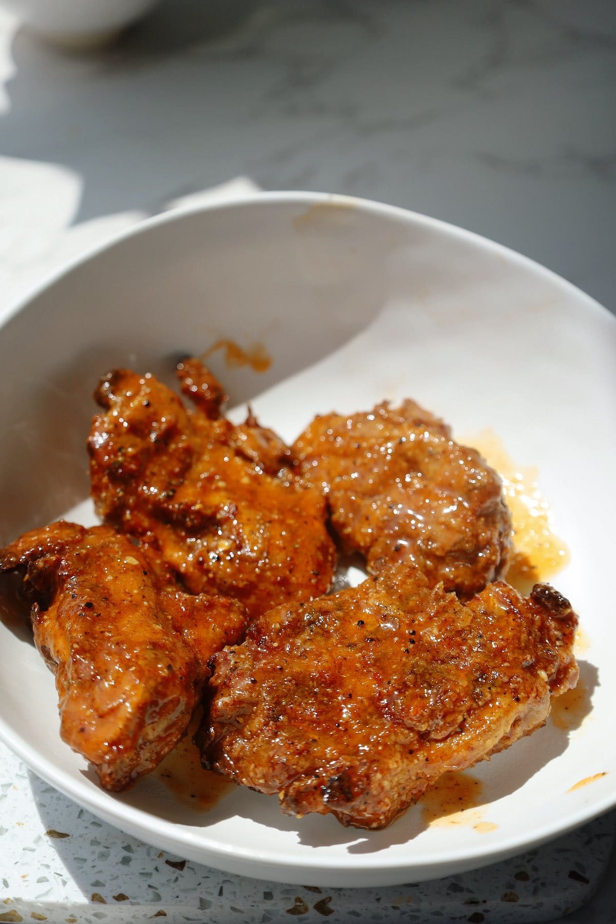Four crispy oyster mushroom lemon pepper wings coated in an orange butter sauce in a white bowl.