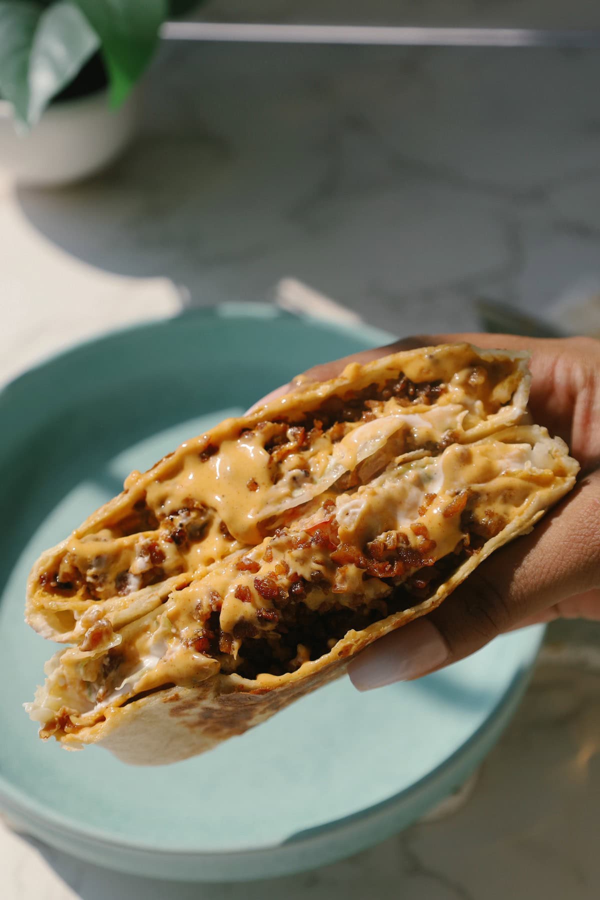 A hand holds a golden toasted vegetarian Crunchwrap Supreme sliced into half.