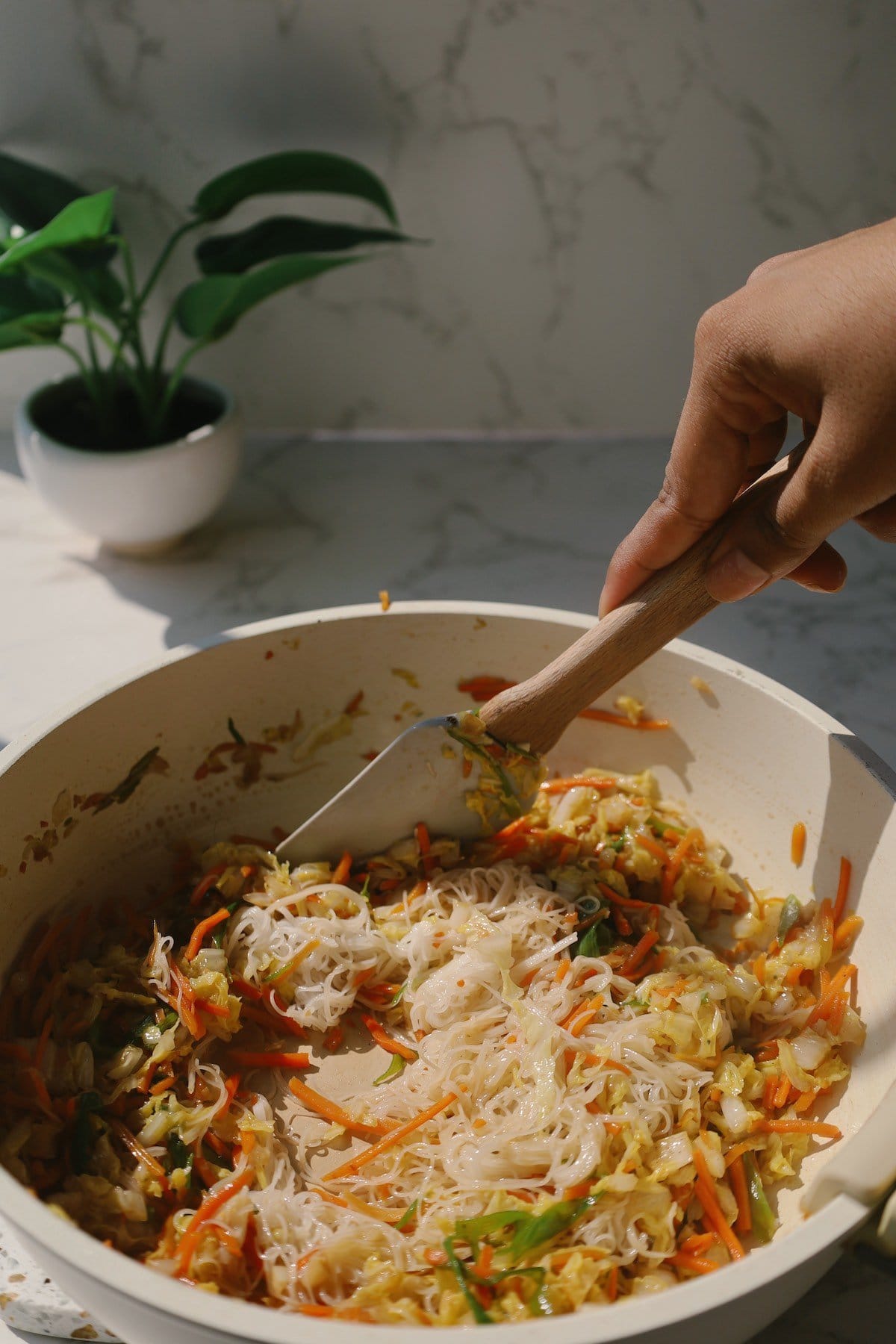 A skillet with sliced carrots, cabbage, scallions, vermicelli noodles and soy sauce being cooked.