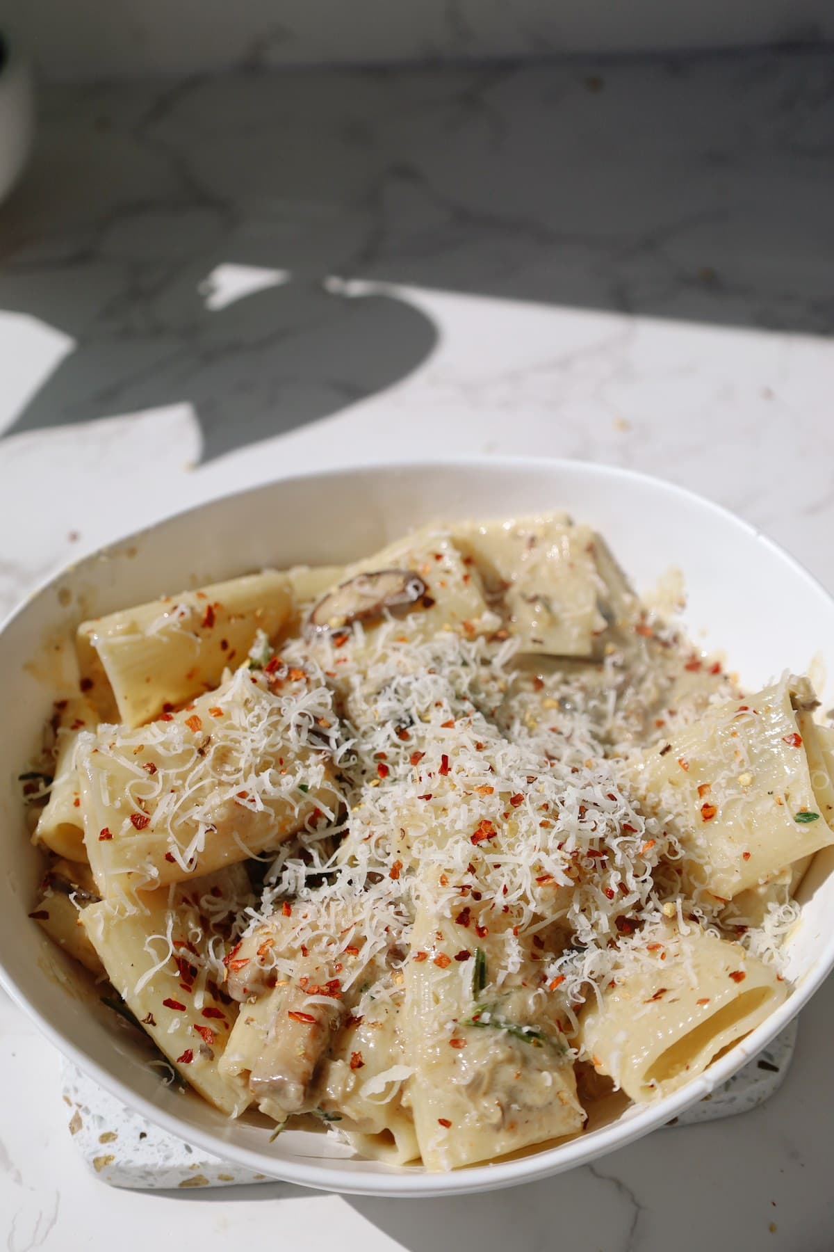A bowl of creamy mushroom miso pasta topped with grated Parmesan and red pepper flakes.