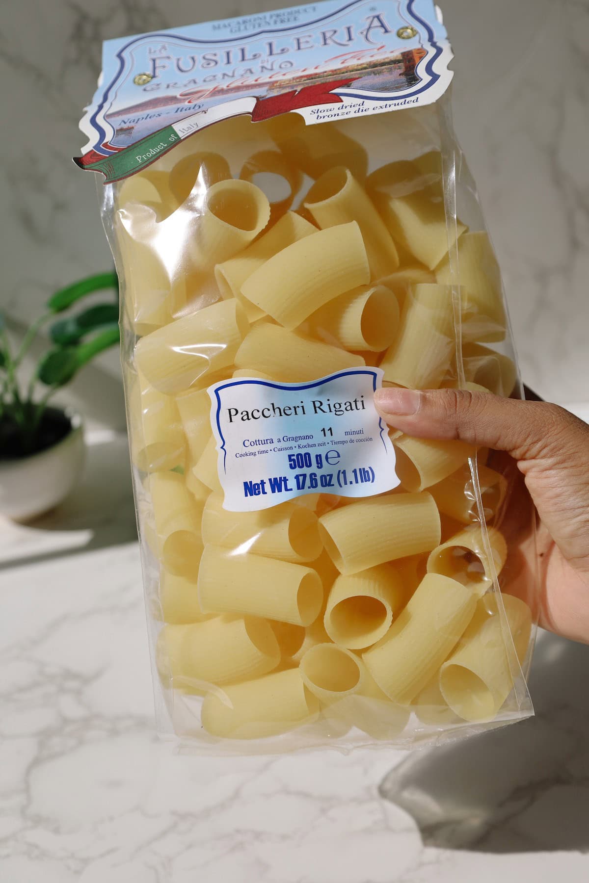 A bag of paccheri rigati pasta is held up beside the ingredients for creamy mushroom miso pasta.