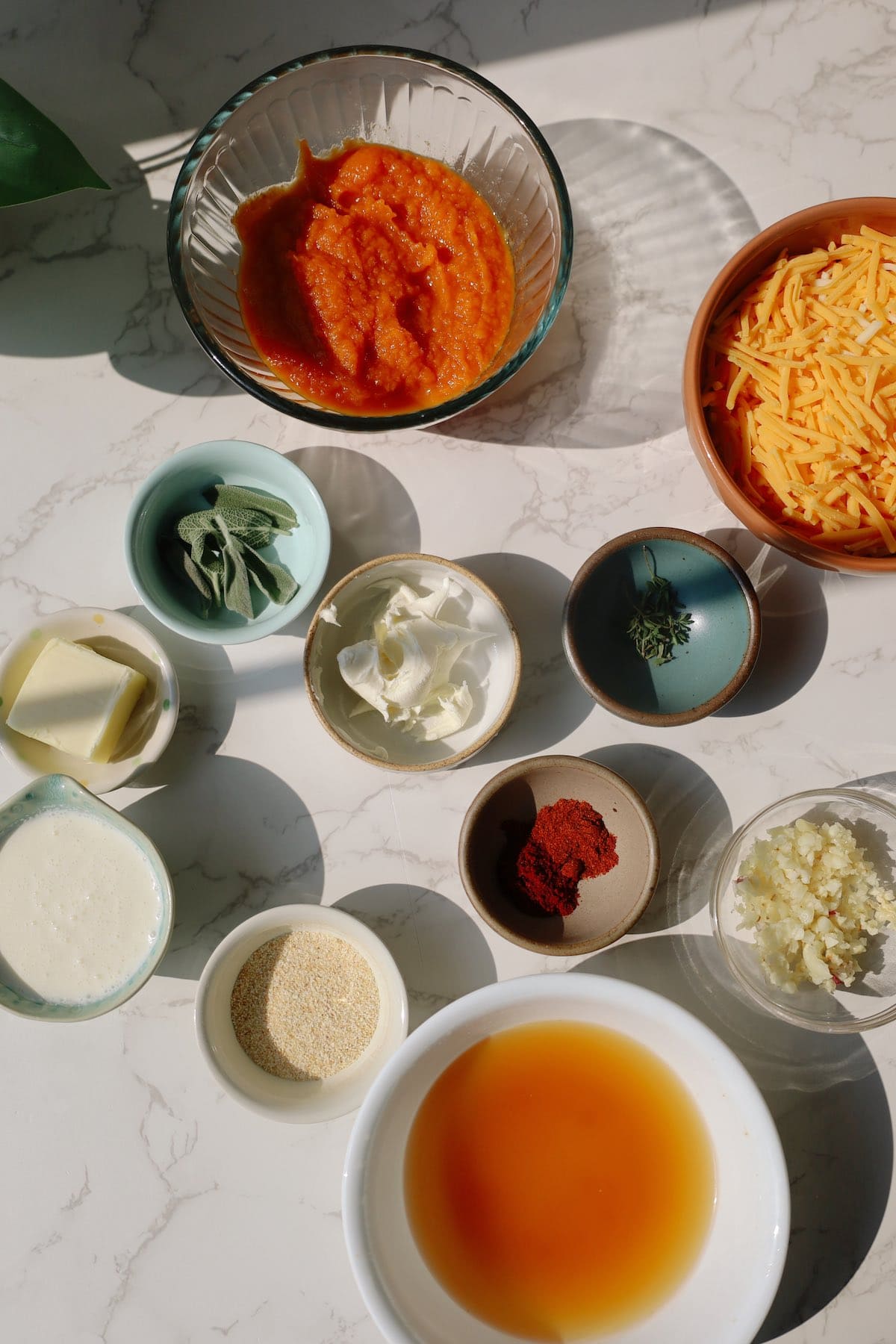 Ingredients for creamy pumpkin pasta including pumpkin purée, shredded cheese, butter, sage, thyme, garlic, cream, spices, and broth.