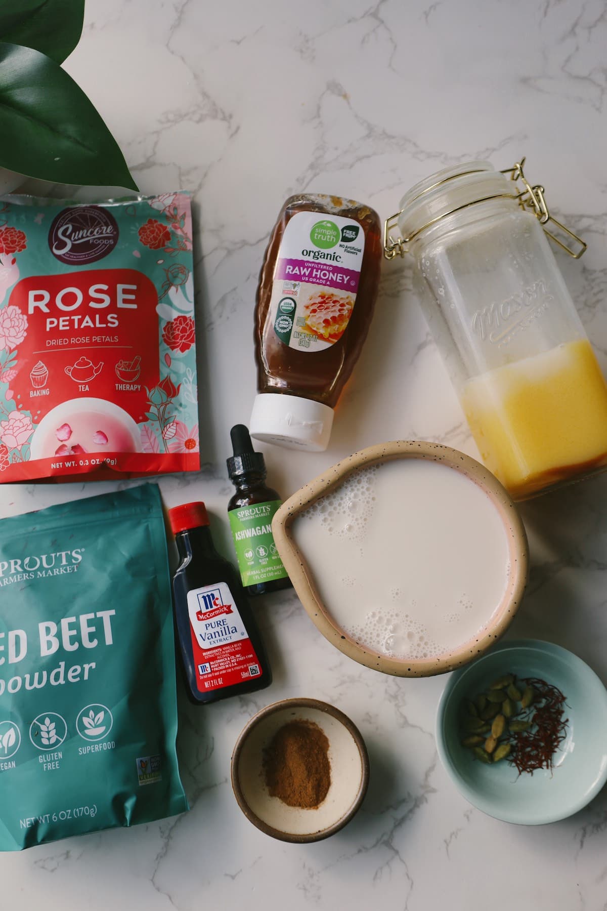Ingredients for pink moon milk including almond milk, honey, ashwagandha tincture, vanilla, beetroot powder, rose petals, cardamom, and spices.