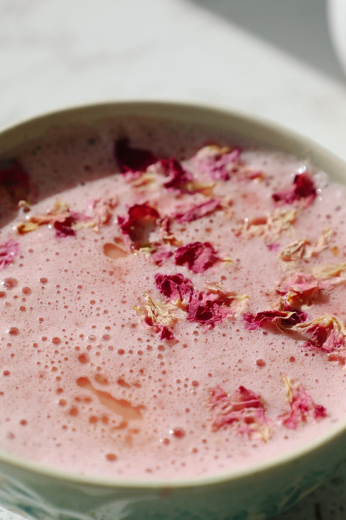 A bowl of pink colored frothy moon milk topped with dried rose petals.