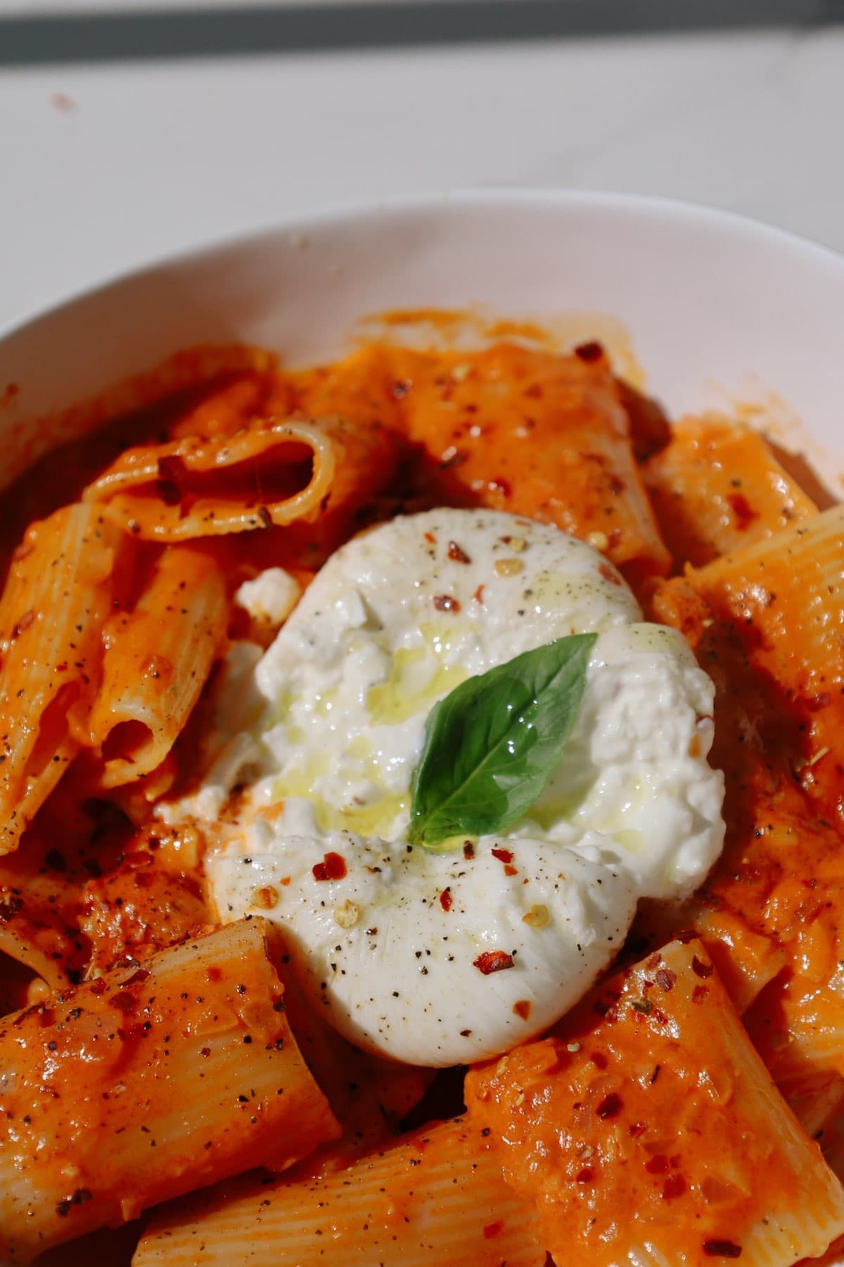 Garnish the spicy rigatoni pasta with burrata and basil.