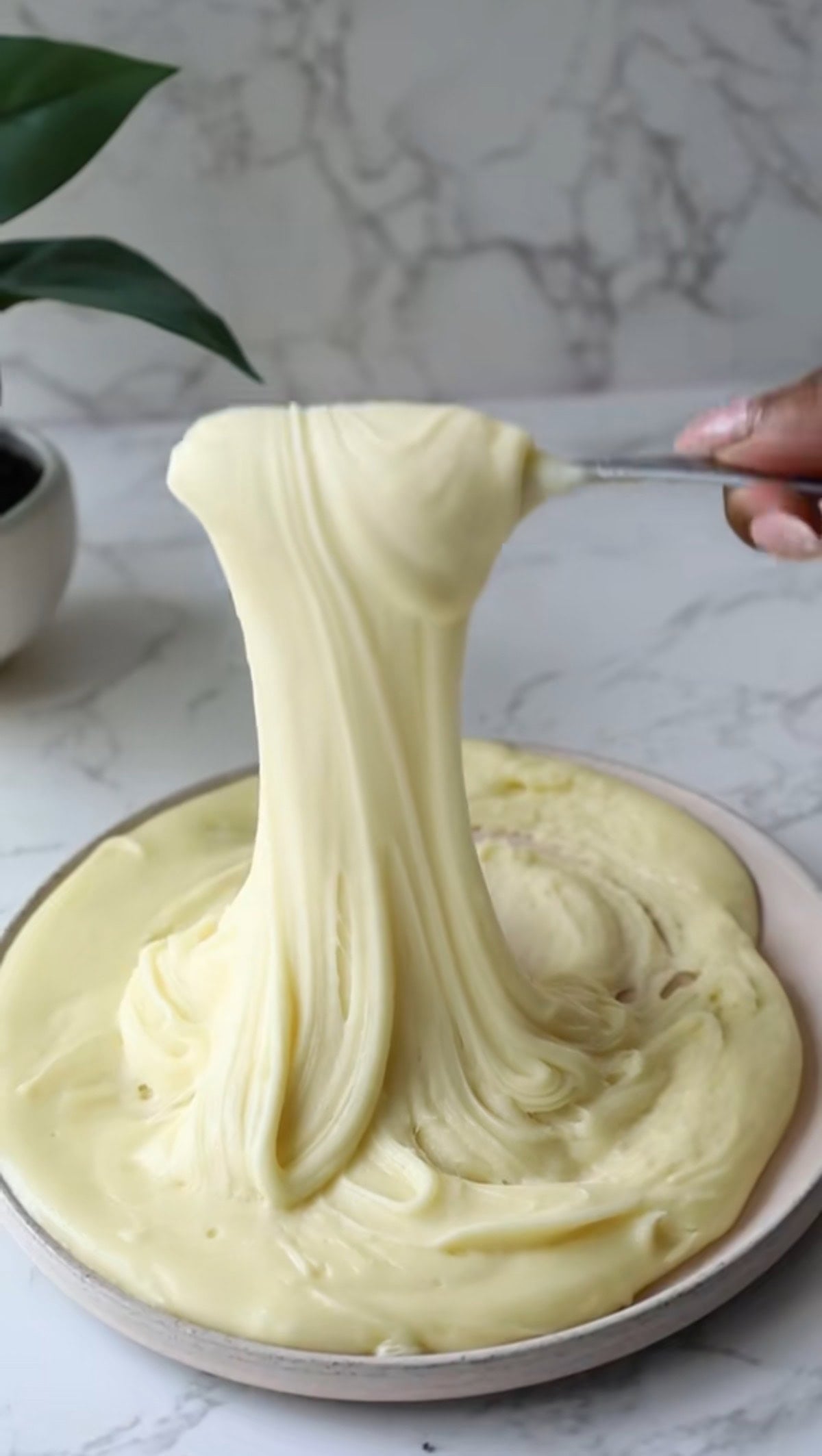 A spoon lifts a long, stretchy ribbon of creamy pommes aligot from a plate.