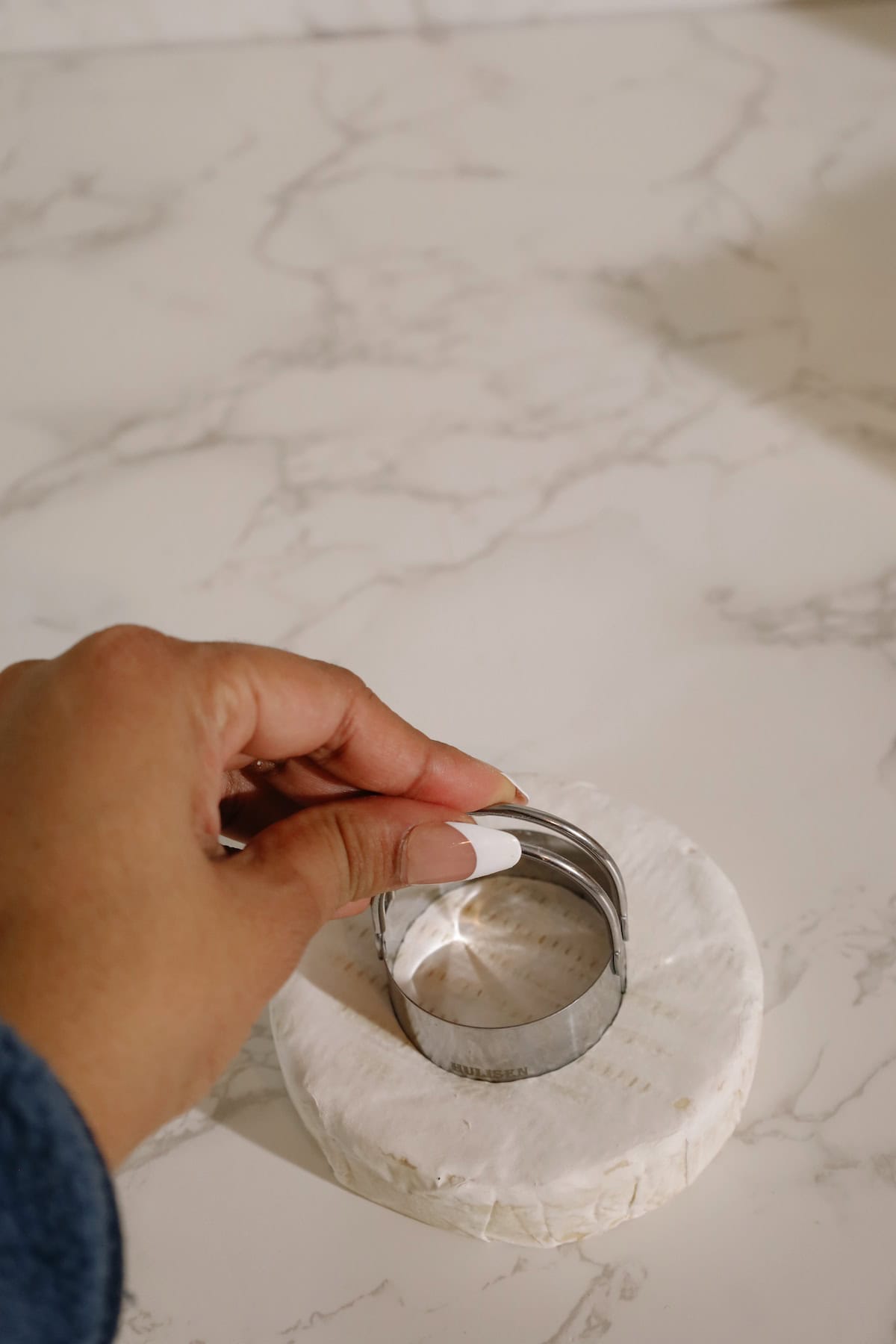 A round cutter is pressed into the center of a brie wheel to create a well for cranberry sauce.