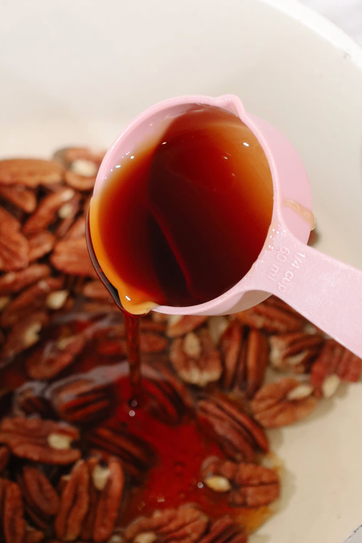 Maple syrup being poured on top of pecans.
