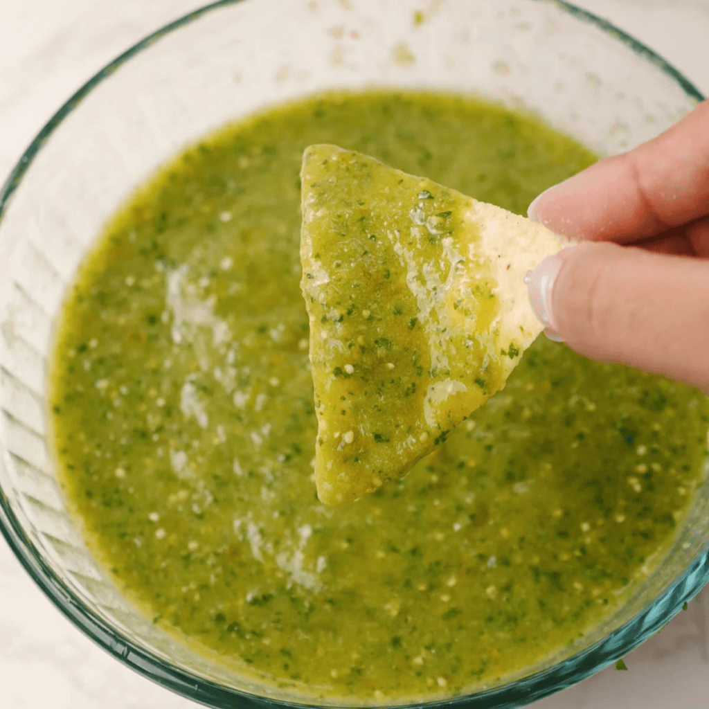 A tortilla chipped dipped into salsa verde.