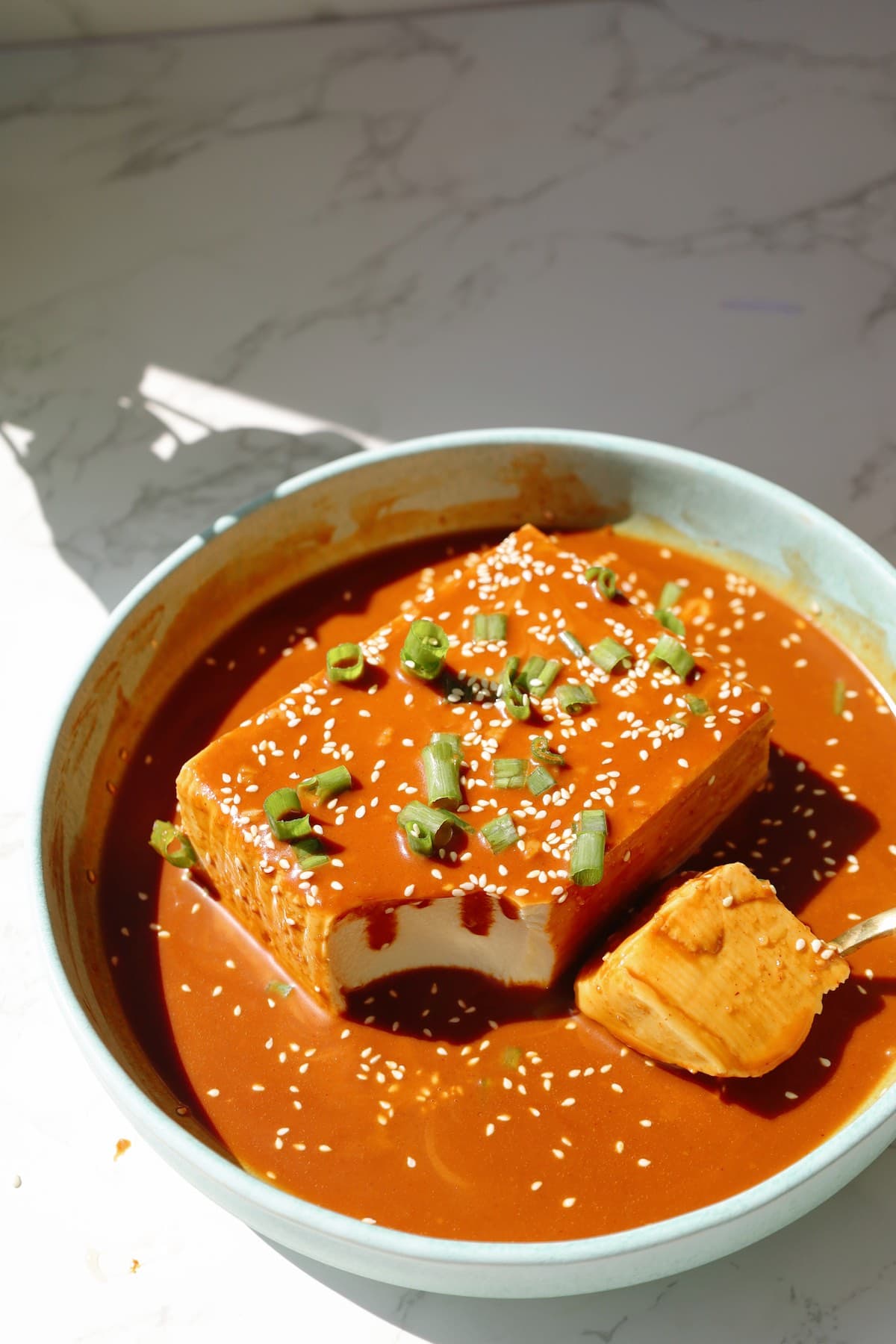 Cold tofu with gochujang peanut sauce on a plate with a bite taken out.