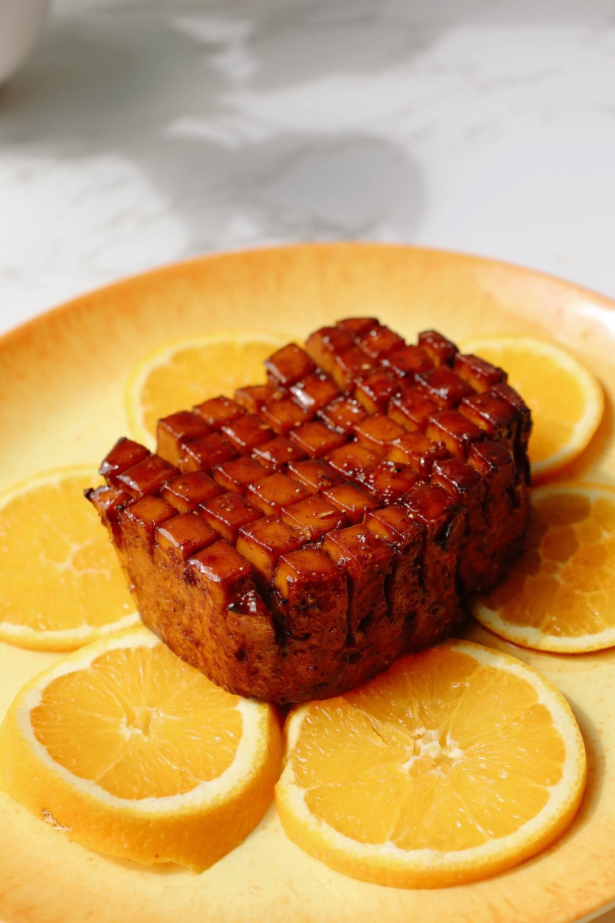 Tofu ham on a yellow plate with some orange slices.