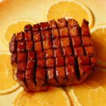 Tofu ham on a plate with orange slices underneath.