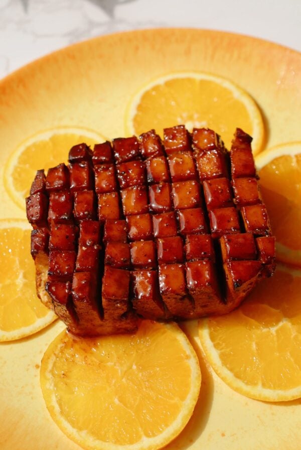Tofu ham on a plate with orange slices underneath.