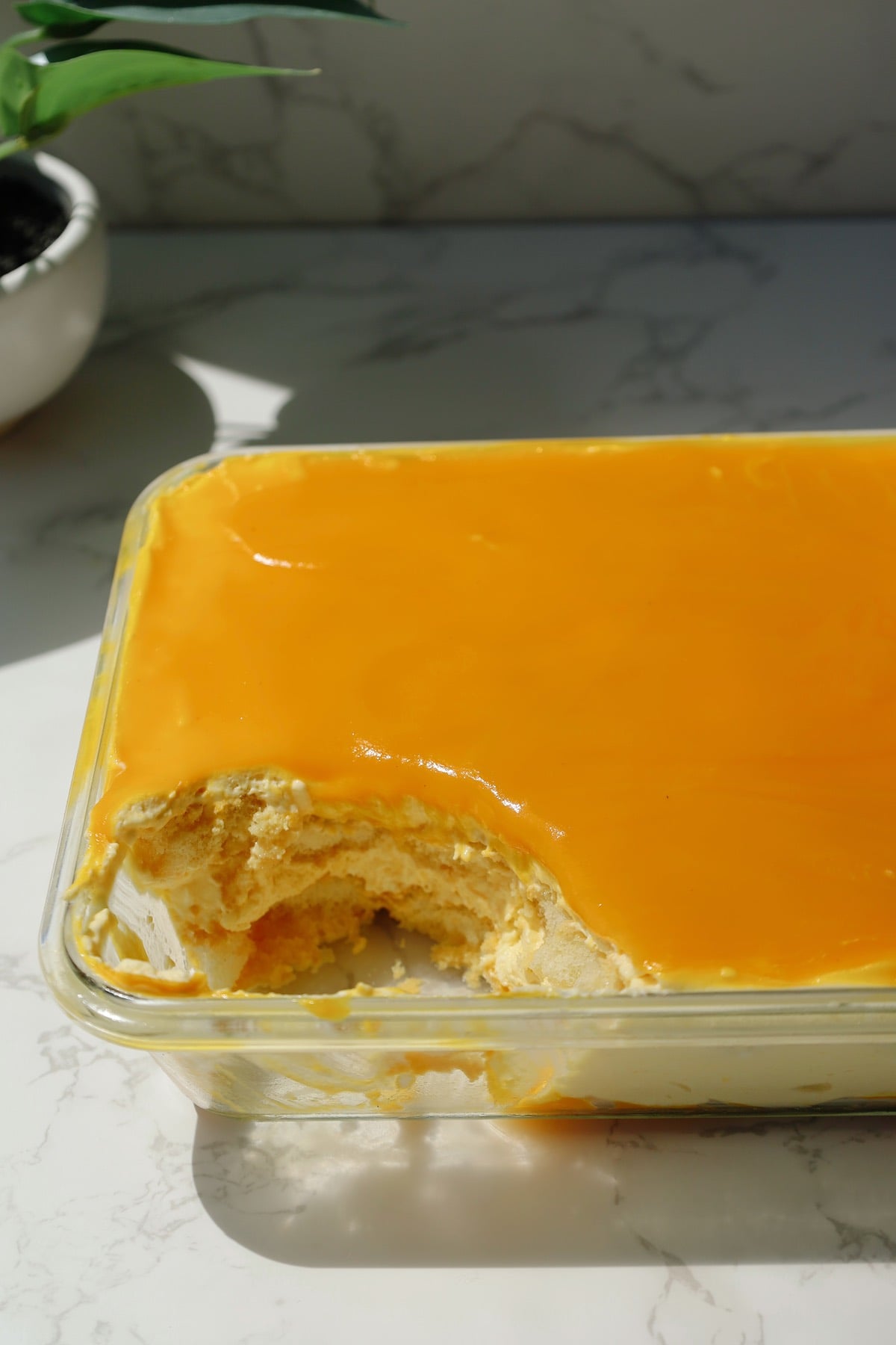 Mango tiramisu in a clear glass dish with a scoop taken out.